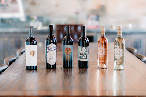 Lineup of 6 wine bottles neatly arranged on a wood table